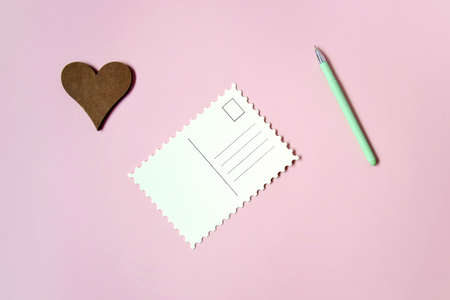 Blank postcard, green ball pen and wooden heart on pink background, empty postcards, postcrossing,...