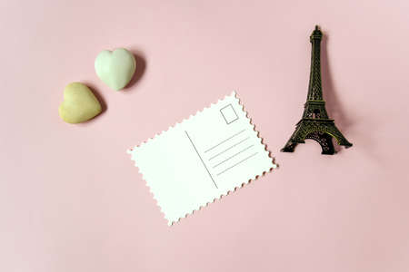 Blank postcard and decorative elements (two stone hearts and a souvenir Eiffel tower) on pink background, empty postcards, postcrossing, mockup. Top view, flat lay. Selective focus. Copy space.の写真素材