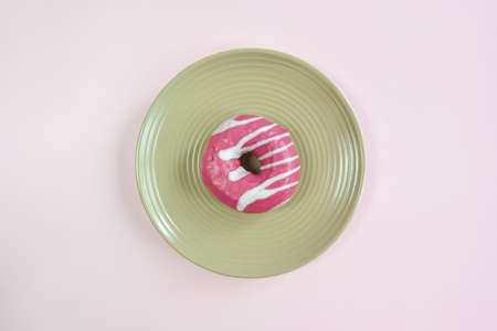 One tasty pink glazed donut on beige round plate on pink background. Top view of appetizing donut. Close-up. Copy space. Selective focus.の写真素材