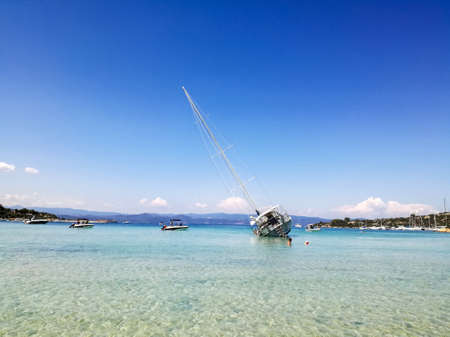 White yacht ran aground and tilted to one side. View of shallow lagoon against blue sky on bright sunny day. Selective focus. Copy space.の写真素材