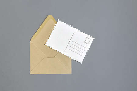 Open empty envelope made of craft paper and unfilled postcard on gray background. Close-up. Top...