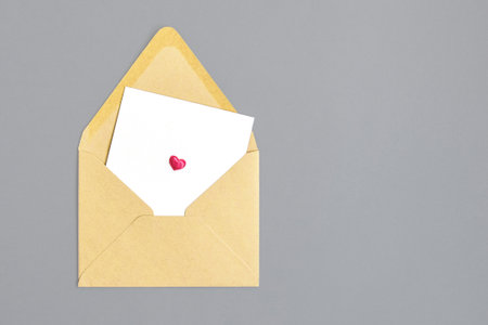 Open empty envelope made of craft paper and white leaf with small pink heart on gray background. Close-up. Top view. Copy space. Selective focus.の写真素材
