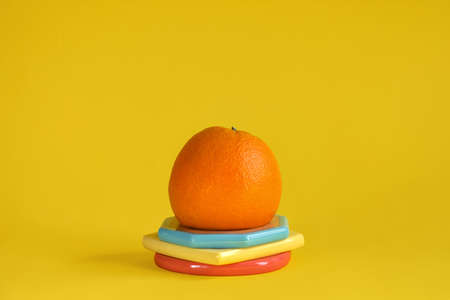 One whole orange on colorful stand on yellow background. Copy space. Selective focus.の写真素材