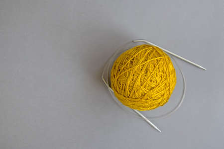 One skein of yellow wool yarn and knitting needles on an gray background, handmade, knitting....