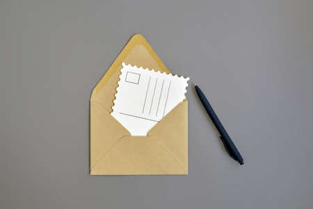 Open envelope made of craft paper, empty postcard and blue ballpoint pen on gray background. Close-up. Top view. Copy space. Selective focus.の写真素材