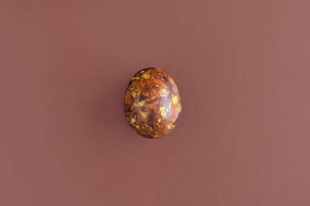 One egg, painted in brown colors, on brown background. Minimalism concept. Unusual pattern on surface of egg in form of blurred spots, handmade. Top view. Copy space.の写真素材