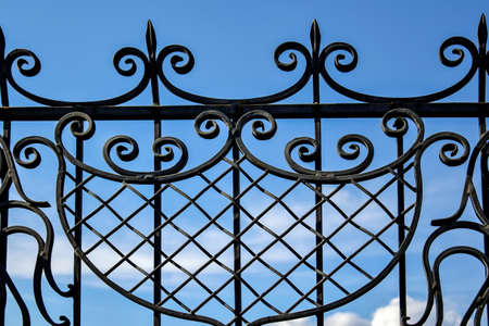 Fragment of black openwork wrought-iron fence grating against blue sky background. Close-up. Copy...