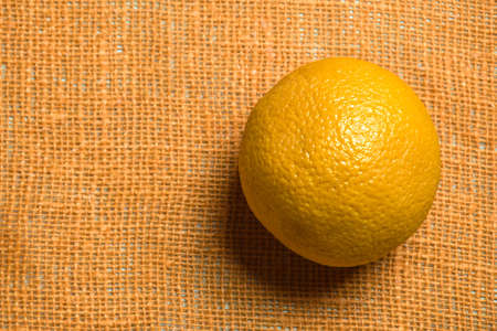 One whole orange on an orange-colored burlap. Close-up. Copy space. Selective focus.の写真素材