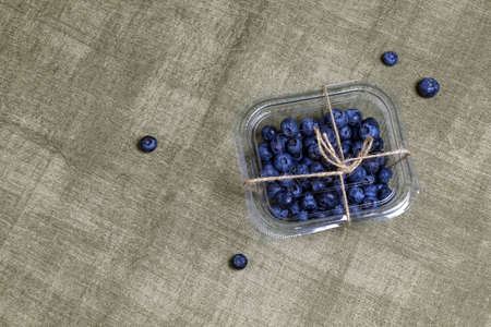 Fresh blueberries in a plastic box tied with string lie on gray textured fabric. Healthy nutrition, diet. Top view. Close-up. Copy space. Selective focus.の写真素材