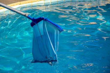 Cleaning pool from garbage with special net. Clear water with blue tint. Concept of hygiene and healthy lifestyle. Horizontal photo. Copy space. Close-up. Selective focus.の写真素材