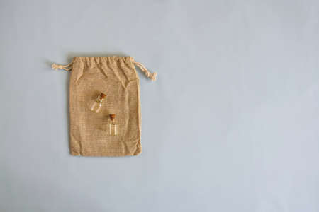 Two empty small glass bottles with stoppers lie on decorative burlap bag on blue background. Top view. Copy space. Selective focus.の写真素材