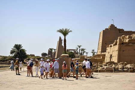 Tourists on excursions in Karnak Temple. Travel tour group near scarab beetle statue. Famous Egyptian landmark with hieroglyphics, decayed temples and obelisks. Luxor, Egypt - October 2021のeditorial素材