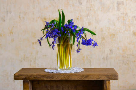 Blue wildflowers in a transparent glass vase on small old wooden table handmade, against background of wall. Rustic lifestyle. close-up. copyspace. selective focus.の写真素材