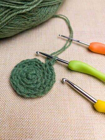 Green yarn thread with and three colorful hooks for knitting and hobbies on gray background from...