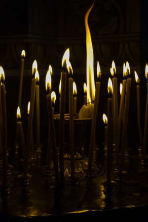 Burning candles in church. Many burning candles shining in dark background. Shallow depth of field.