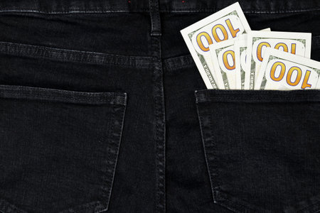 Stack of hundred bills in back pocket of black dollar jeans, denim background texture. Spending Money. close-up.の写真素材