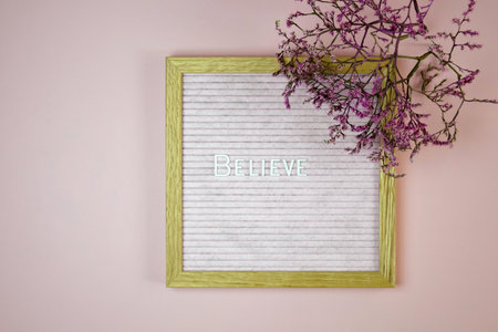 Word BELIEVE from white letters on letter board and branch of pink dried flower on pink background. top view. copyspace. selective focus.の写真素材