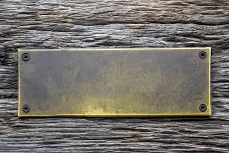 Antique blank brass rectangular plaque screwed with rusty screws to an old weathered board with deep wrinkles. Place for text on bronze plate. Copy space. Close-up. Mock-up.の写真素材