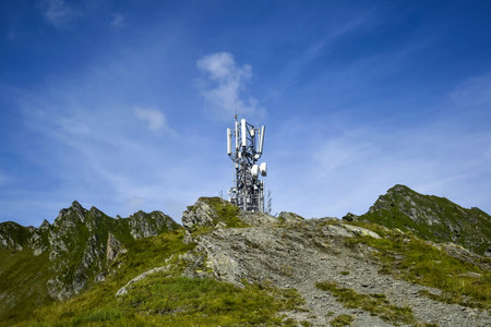 Metal tower with various telecommunication antennas on top of a mountain, against a background of...