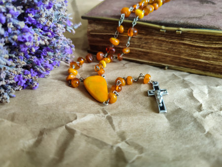 Amber rosary lies gracefully next to an aged prayer book, with colorful bouquet of dried lavender nearby, all resting on crumpled craft paper. Copy space. Close-up.の写真素材