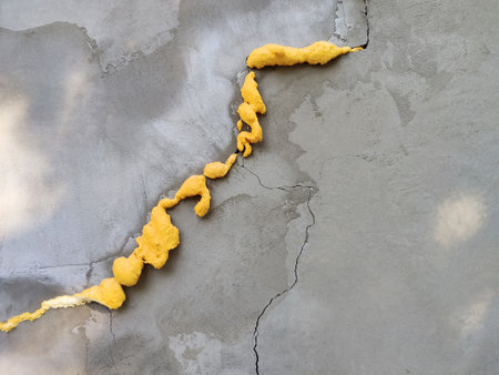 Winding crack in plastered concrete gray wall sealed with yellow construction foam. Temporary solution to the problem, repair of damage. Copy space for text.の写真素材