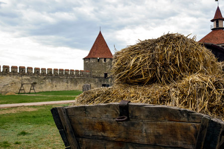 Old wooden cart with bales of hay against background of stone walls of ancient medieval fortress....