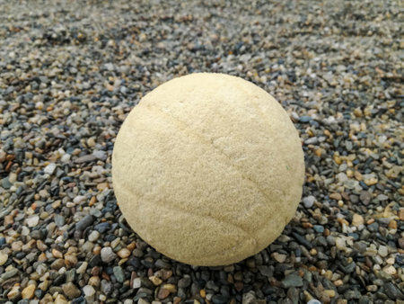 Old worn out faded ball against background of small multi-colored pebbles. Close-up. Copy space. Selective focus.の写真素材