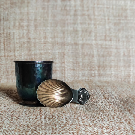 Silver cup with patina and spoon in shape of shell. Vintage silverware darkened by time. Placed on background of gray fabric. Close-up. Copy space for text.の写真素材