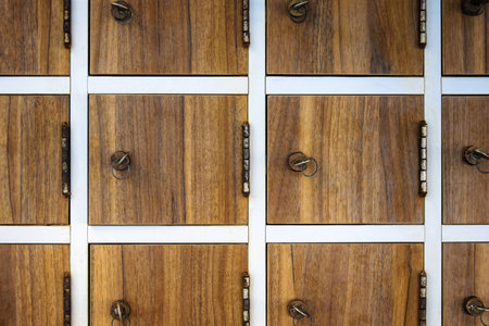 Old storage system with small compartments that lock with key. Keys with rings are inserted into locks in wooden doors, rusty hinges. Selective focus. Copy space for text.の写真素材