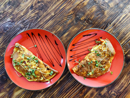 Omelette decorated with greens on red ceramic plates placed on dark surface of wooden vintage table. Simple, tasty and healthy food. Great breakfast. Top view. Close-up. Selective focus. Copy space.の写真素材