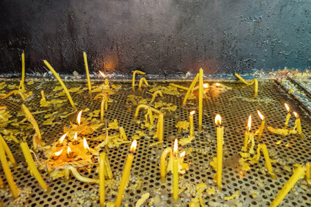 Lighted melted church wax candles thrust into perforated metal plate on stand on black background. Burning candles in church. Close-up. Selective focus. Copy space.の写真素材