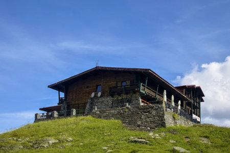 Large old wooden house on high stone foundation on top of green rocky hill, mountain. Against...