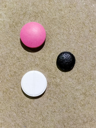 White, black and pink medical pill on beige wood fiber board. Concept of medicine and pharmacy. Top...