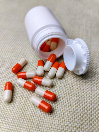 Two-color medicinal capsules in gelatin shell spilled out of plastic jar. Medical pills in open...
