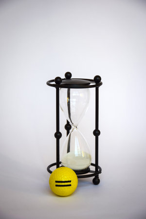 Hourglass with yellow golf ball on light background. Time for game of golf. Sandglass in black black...