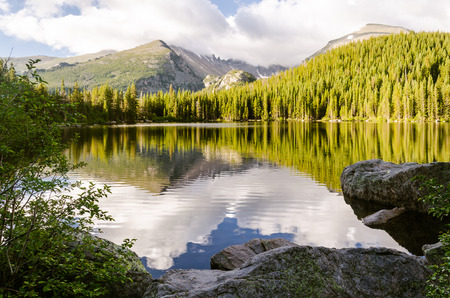 landscape of a glacial lake with sorrounded by mountain peak and forrest that mirrored in the water surfaceの写真素材