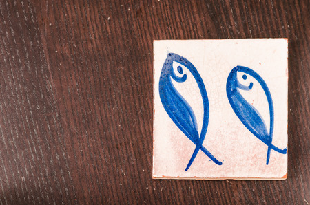 tile with fishes drawing on it over a wooden tableの写真素材