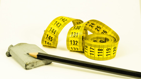 still life with a yellow tape measure, a black pencil and rubber, over whiteの写真素材