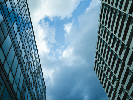 two buildings cover almost all the view of the sky, clouds are over me but a spot of  blue sky makes me hopefulの写真素材