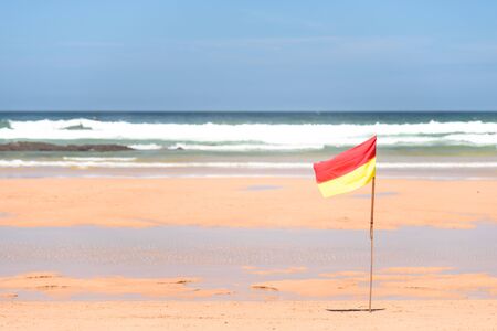 a red yellow flag waves in front of the ocean. alert, message.の写真素材