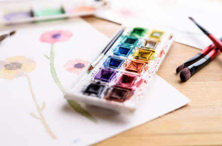 paint palette and paintbrushes and a watercolor flower painting on paperの写真素材