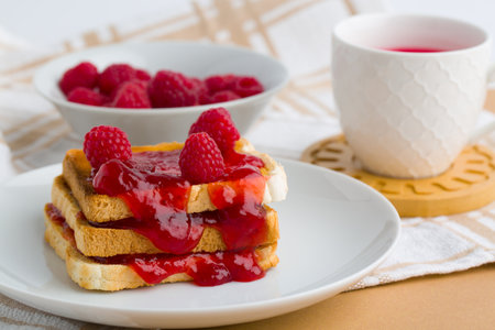 Toast with raspberry jam and cup of tea on beige table.の写真素材