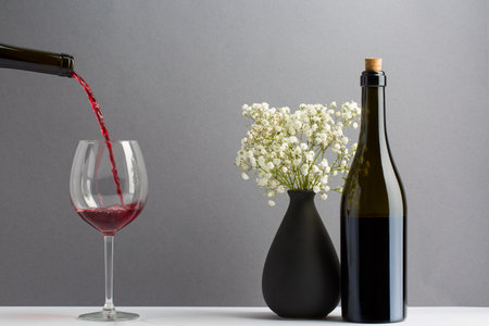 elegant red wine bottle pour glass, vase with small white flowersの写真素材