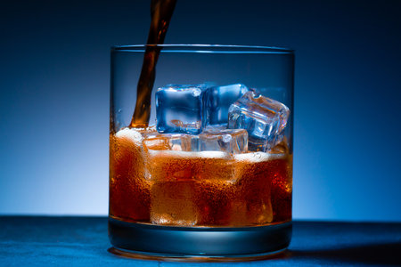 Glass of cola with ice cube on a blue backgroundの写真素材