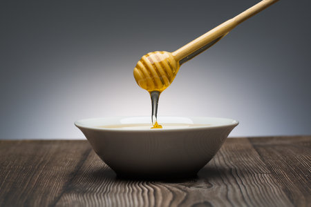 honey drips from the spoon into a white bowl still lifeの写真素材
