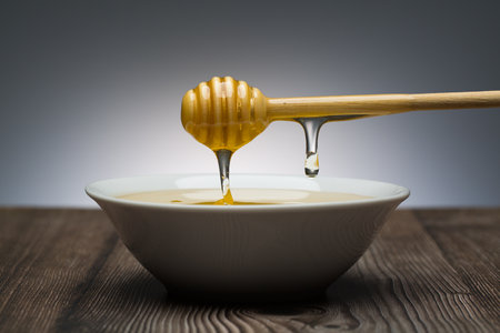 honey drips from the spoon into a white bowl still lifeの写真素材
