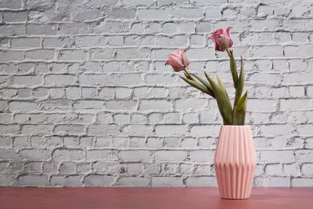 Pink tulips in vase on wooden table against white brick wallの写真素材