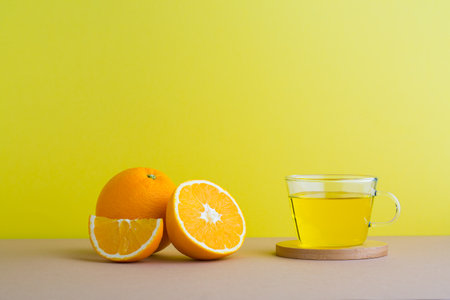 Orange juice in a glass cup and fresh orange on a yellow backgroundの写真素材