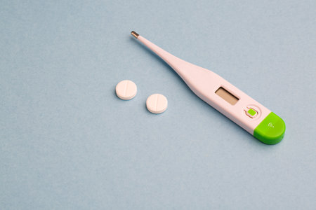 Medical thermometer and pills on a blue background. Top view.