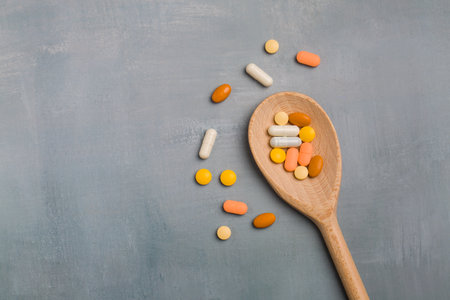 Colorful pills in wooden spoon on gray background. Top view.の写真素材